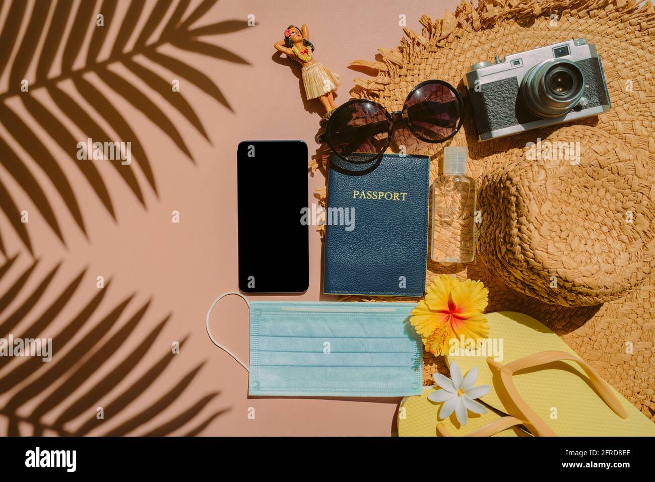 Essenziale per il viaggio da portare in volo durante la pandemia del coronavirus. Posa piatta di telefono, passaporto, maschera facciale, bottiglia igienizzante per le mani, infradito, fotocamera Foto Stock