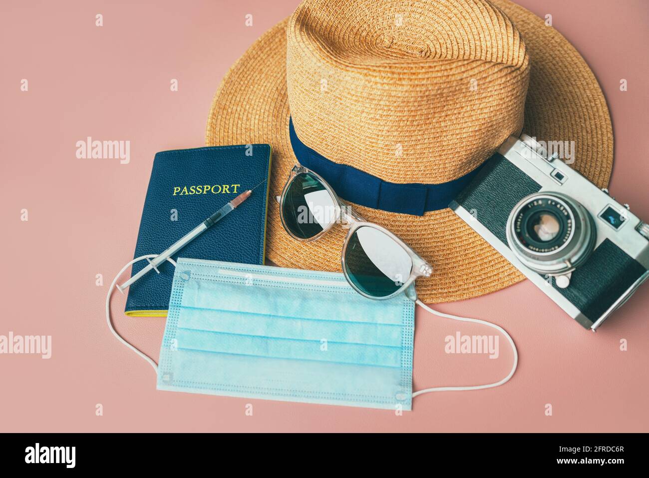 Il passaporto del vaccino del coronavirus ha bisogno di viaggio : macchina fotografica, cappello, occhiali da sole, maschera facciale su sfondo rosa. Corona certificato virus prova fortravelers Foto Stock
