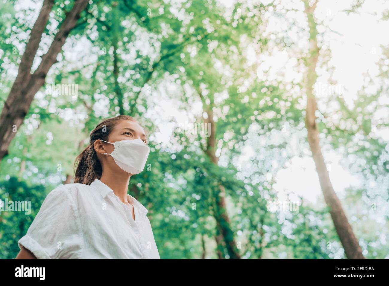 Maschera indossando la donna che guarda al futuro luminoso nella speranza  che cammina nella foresta. Tessuto di moda sostenibile in PPE, stile di  vita ragazza asiatica respirando aria pulita Foto stock -