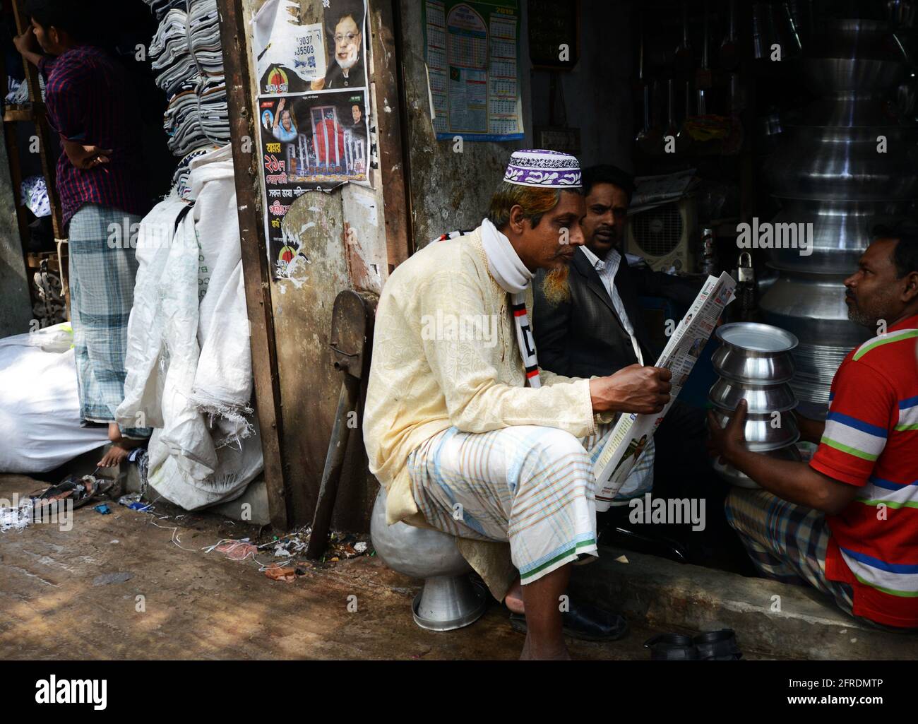 Un uomo del Bangladesh che legge il giornale da un piccolo negozio di penteria al bazar di Chowk nella vecchia Dhaka, Bangladesh. Foto Stock