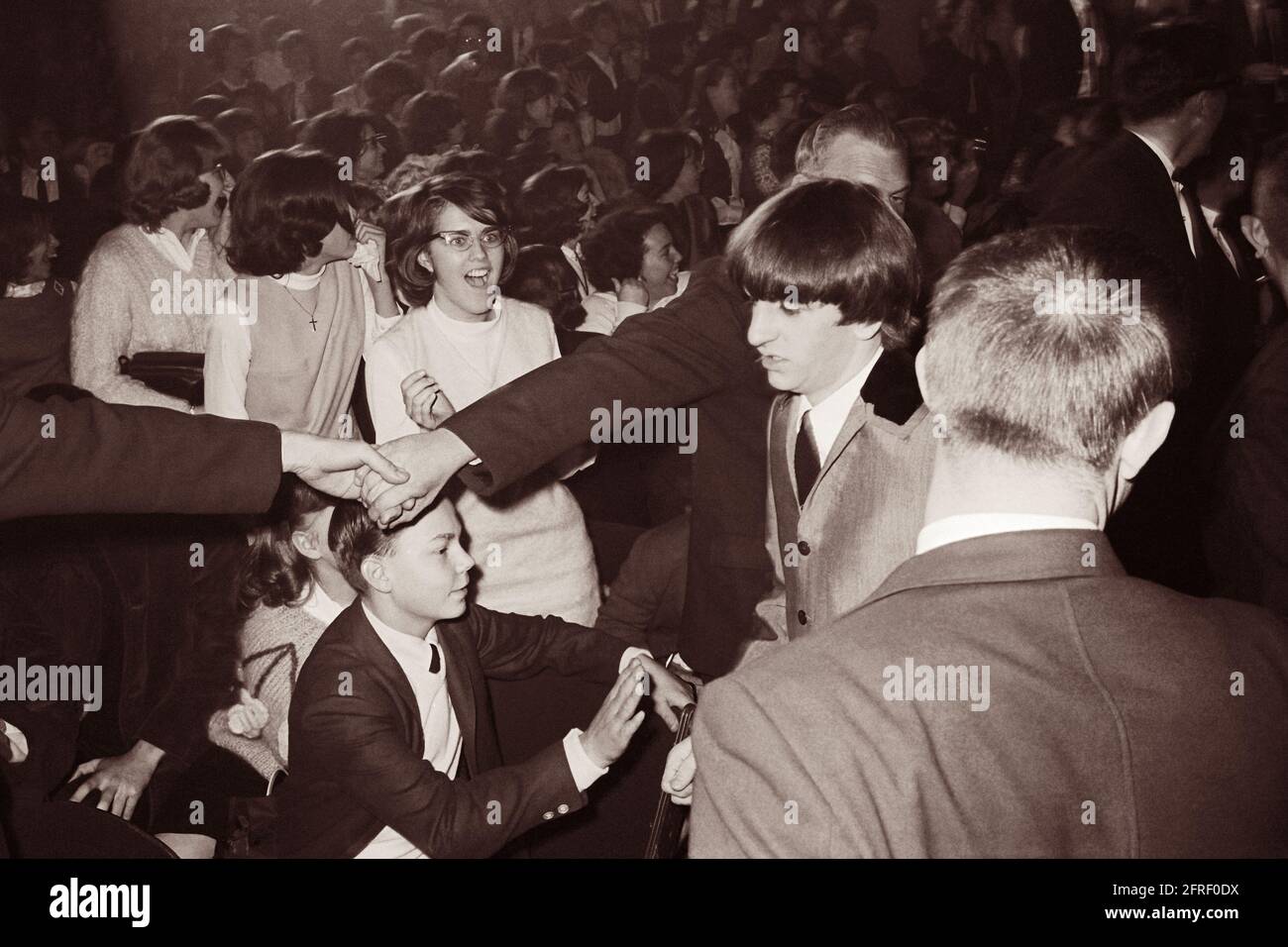 La polizia si univa alle mani per tenere indietro i fan adoranti mentre Ringo Starr cammina al Washington Coliseum di Washington, D.C., dove i Beatles stavano suonando nel loro primo concerto americano il 11 febbraio 1964. (STATI UNITI) Foto Stock
