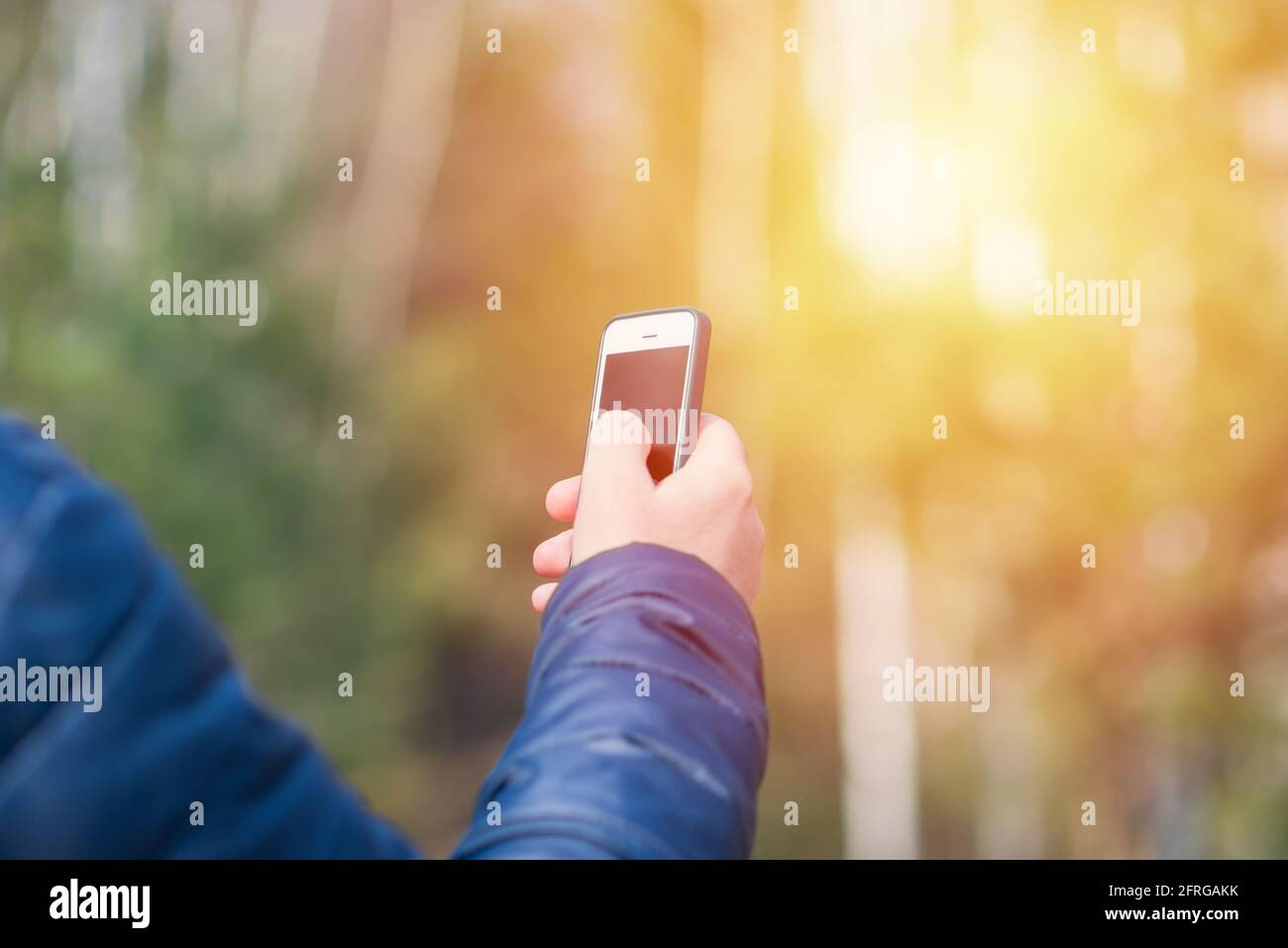 Un uomo con il suo smartphone cellulare alla ricerca del segnale di ricezione nella foresta primaverile soleggiata. Foto Stock