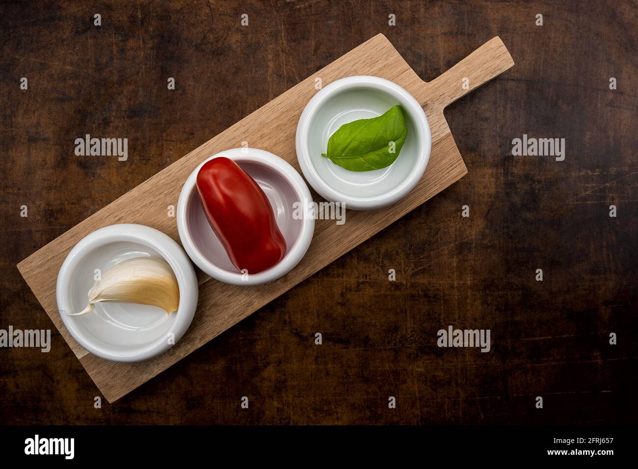 Aglio, mini pomodoro e foglia di basilico in piccole ciotole bianche in porcellana su tavola di legno. Foto Stock