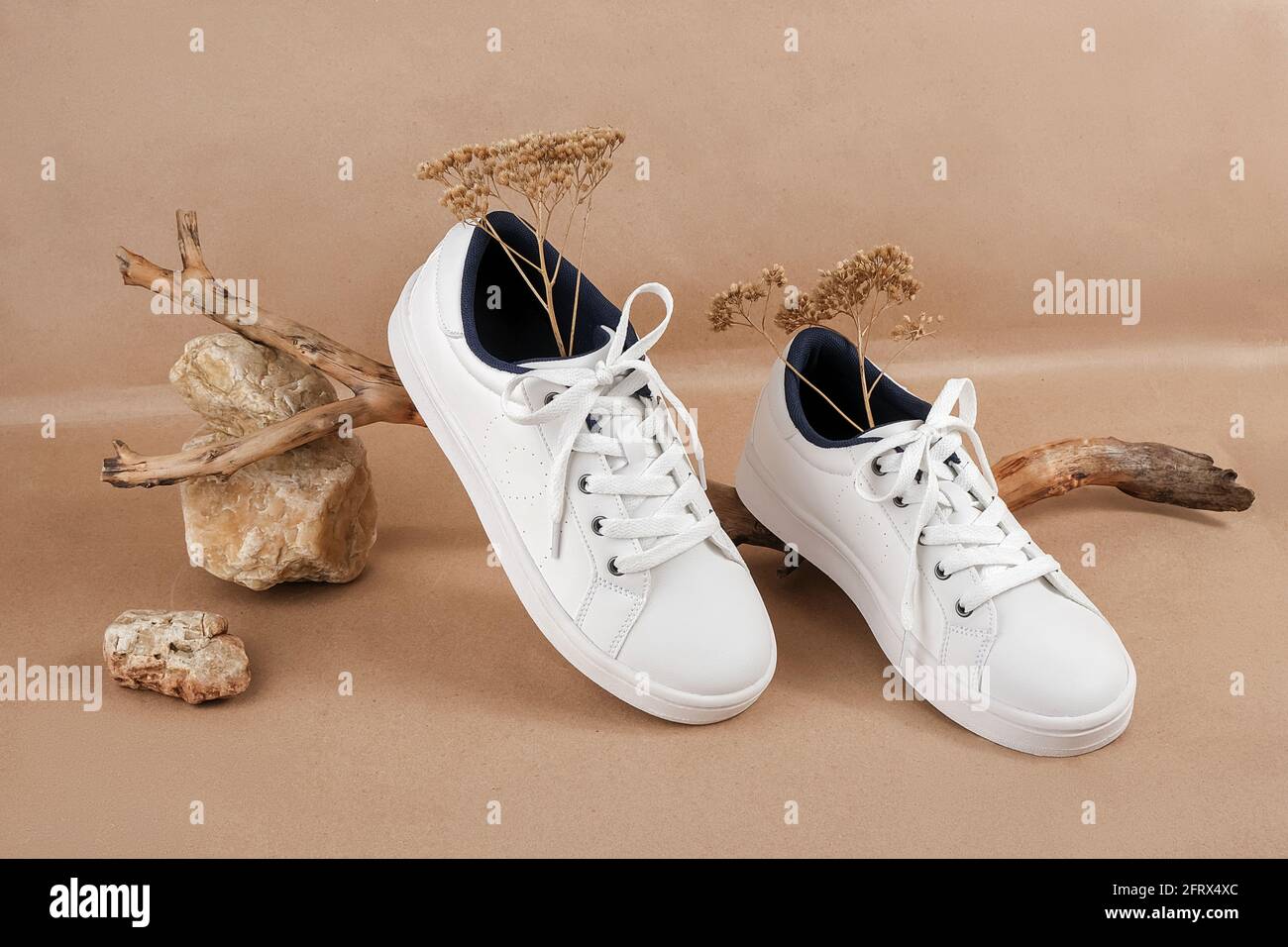 Concetto etico di scarpe vegan. Un paio di sneakers bianche con fiori  secchi sul legno e mucchio di pietre, fondo carta da artigianato beige  neutro Foto stock - Alamy