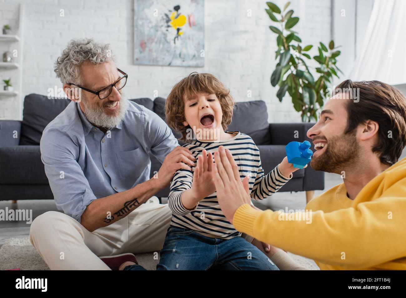 Sorridendo padre e figlio con blocchi di costruzione dando alto cinque vicino nonno Foto Stock