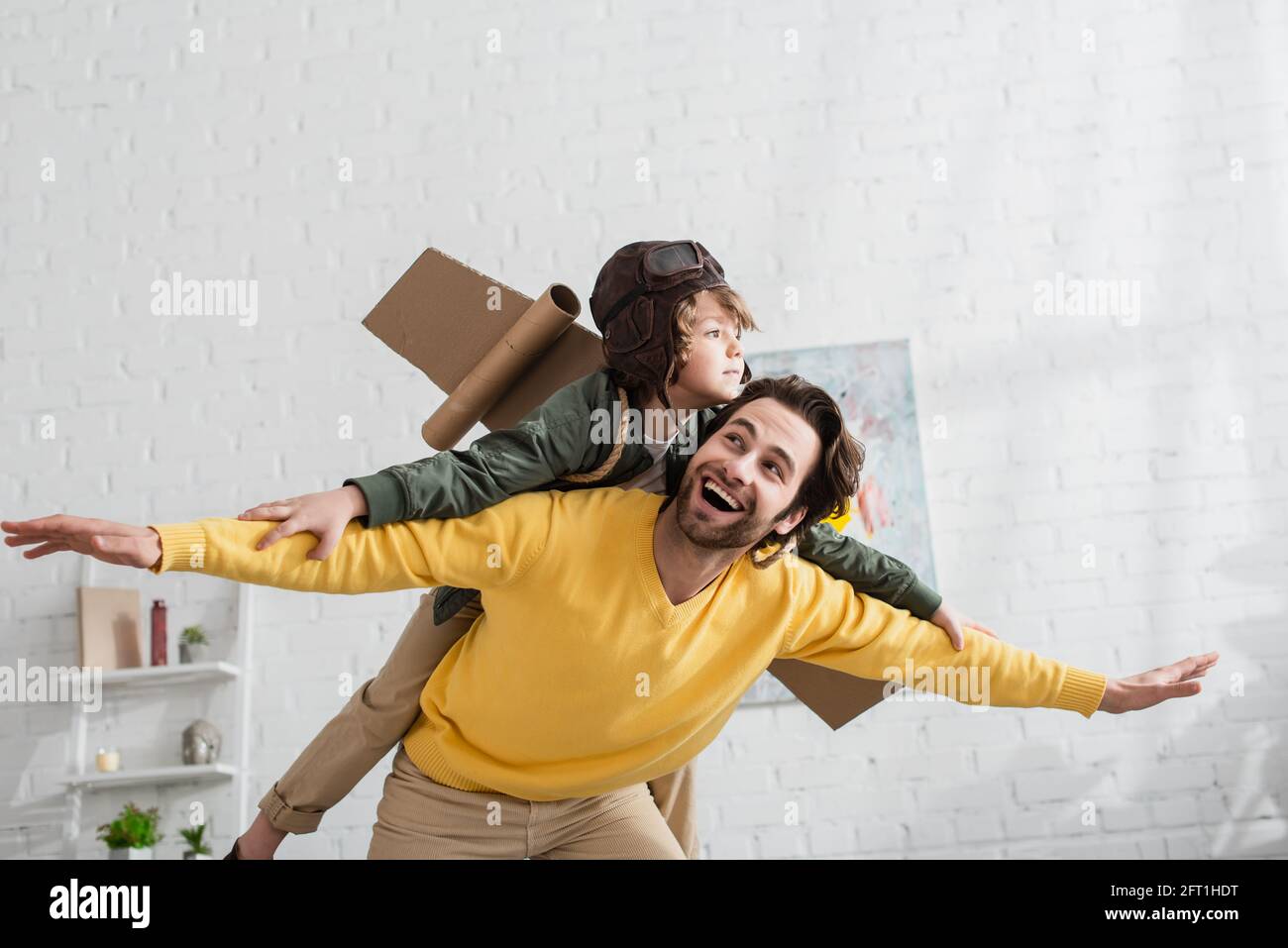 Sorridente padre che gioca con su in casco aviatore e ali Foto Stock