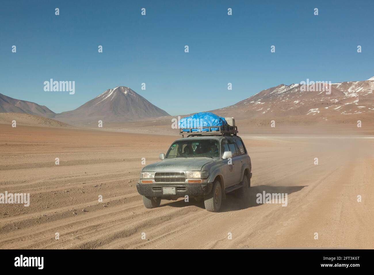 Sullo sfondo di vulcani, un veicolo fuoristrada 4x4 attraversa il paesaggio desertico della Bolivia in un safari turistico terrestre. Foto Stock