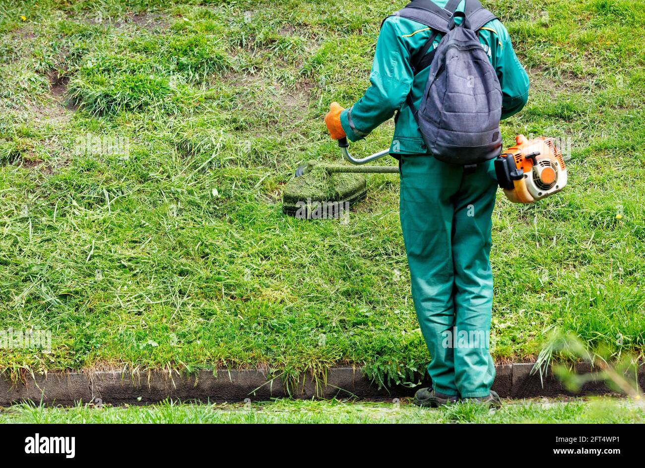 Un operaio in tute verdi e uno zaino sulla schiena falda l'erba con un  trimmer industriale a benzina in un parco cittadino. Spazio di copia Foto  stock - Alamy