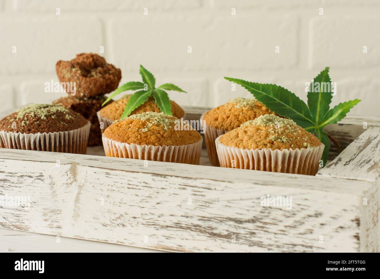 Muffin sani e gustosi privi di glutine e vegani, conditi con semi di canapa su un piatto bianco su un tavolo di legno. Muffin alla tazza di marijuana con congedo di cannabis Foto Stock