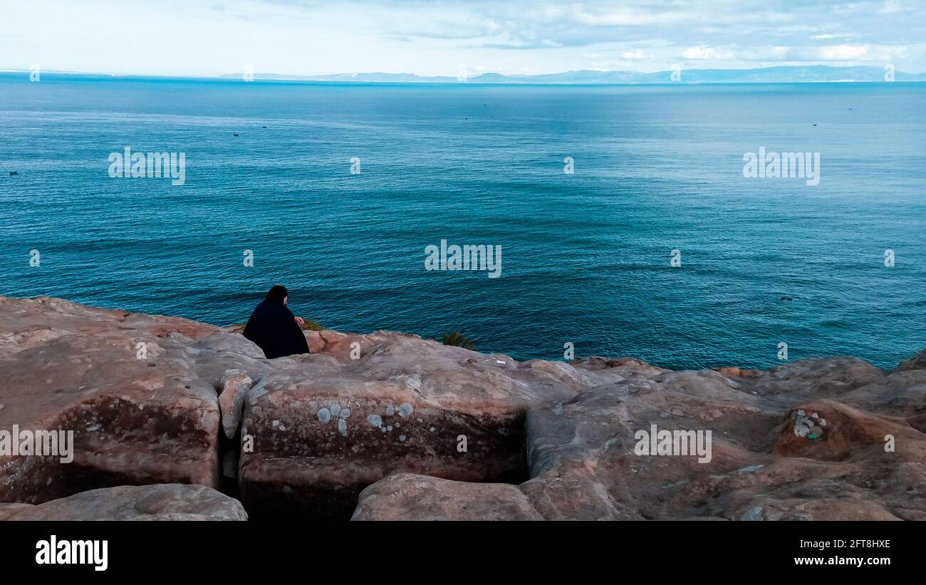 Una donna in abito islamico si siede da sola e si affaccia su una splendida vista del Mar Mediterraneo. Foto Stock