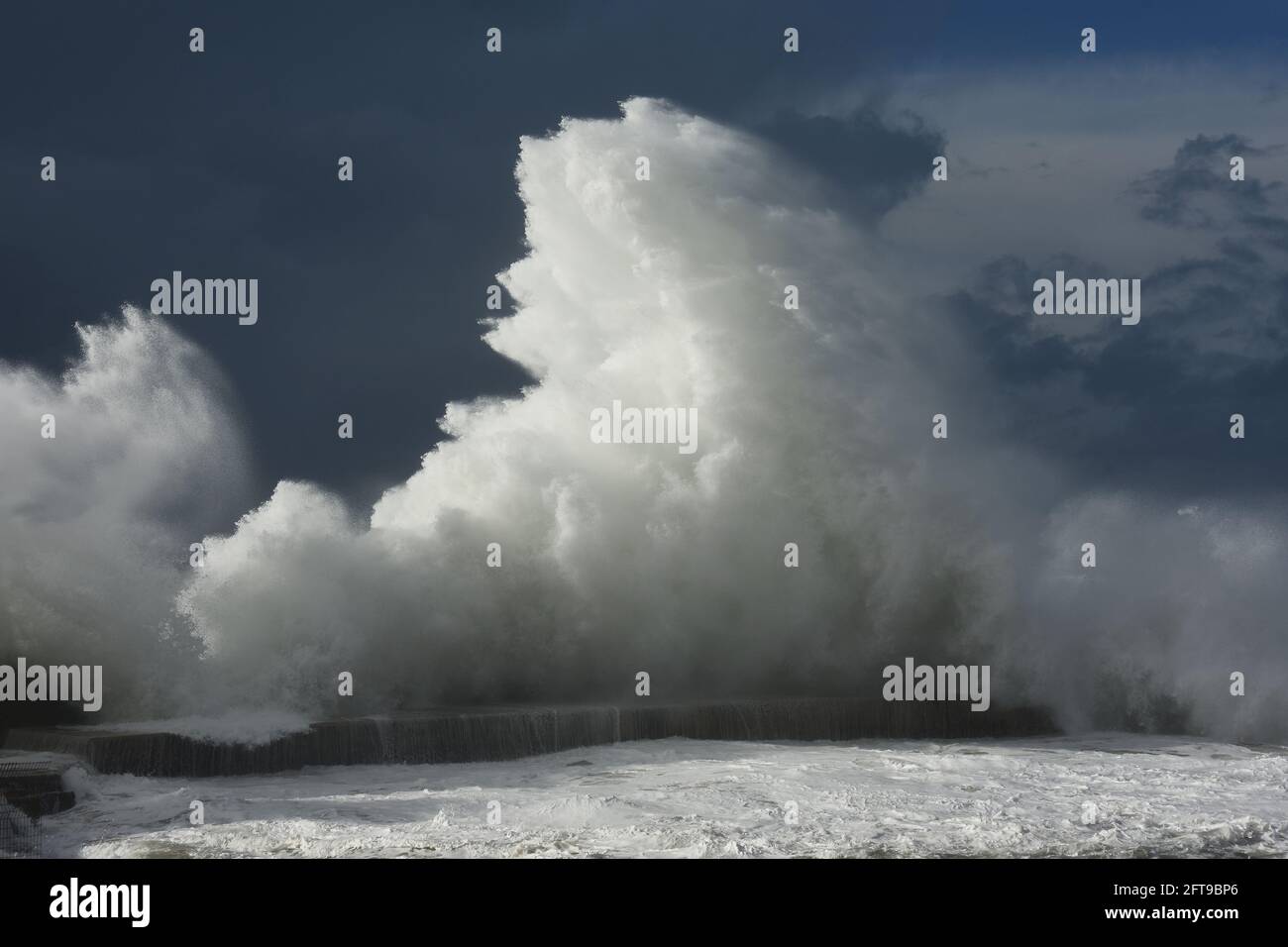 La rottura dell'onda su una torta di pietra rin un inverno tempestoso giorno/ Foto Stock