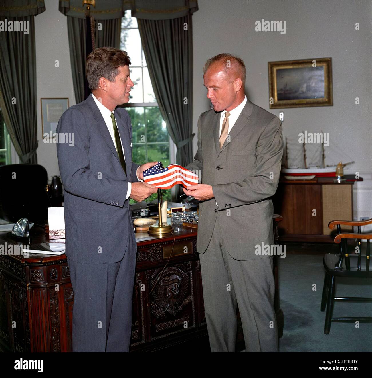 Il presidente John F. Kennedy riceve un dono di una bandiera americana dall'astronauta tenente colonnello John H. Glenn, Jr. (A destra); il Lt. Colon ha portato la bandiera nella sua tuta spaziale durante il suo volo orbitale a bordo del Mercury-Atlas 6, noto anche come amicizia 7. Sullo sfondo c'è l'assistente speciale del presidente, Kenneth P. o'Donnell. Ufficio ovale, Casa Bianca, Washington, D.C. Foto Stock