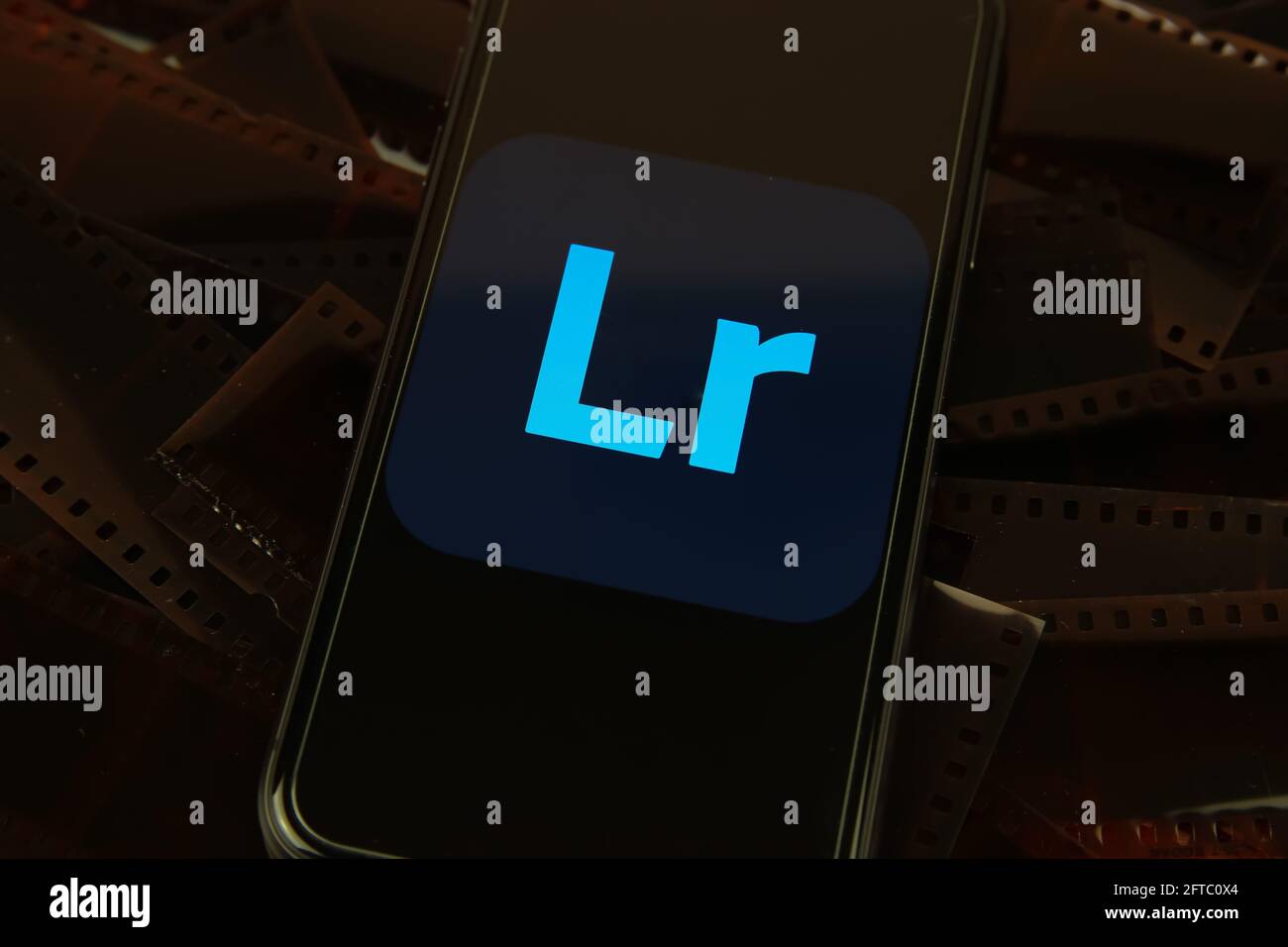 Viersen, Germania - 9 maggio. 2021: Primo piano dello smartphone con la scritta con il logo del programma di editing di foto adobe lightroom su strisce di pellicola negative Foto Stock