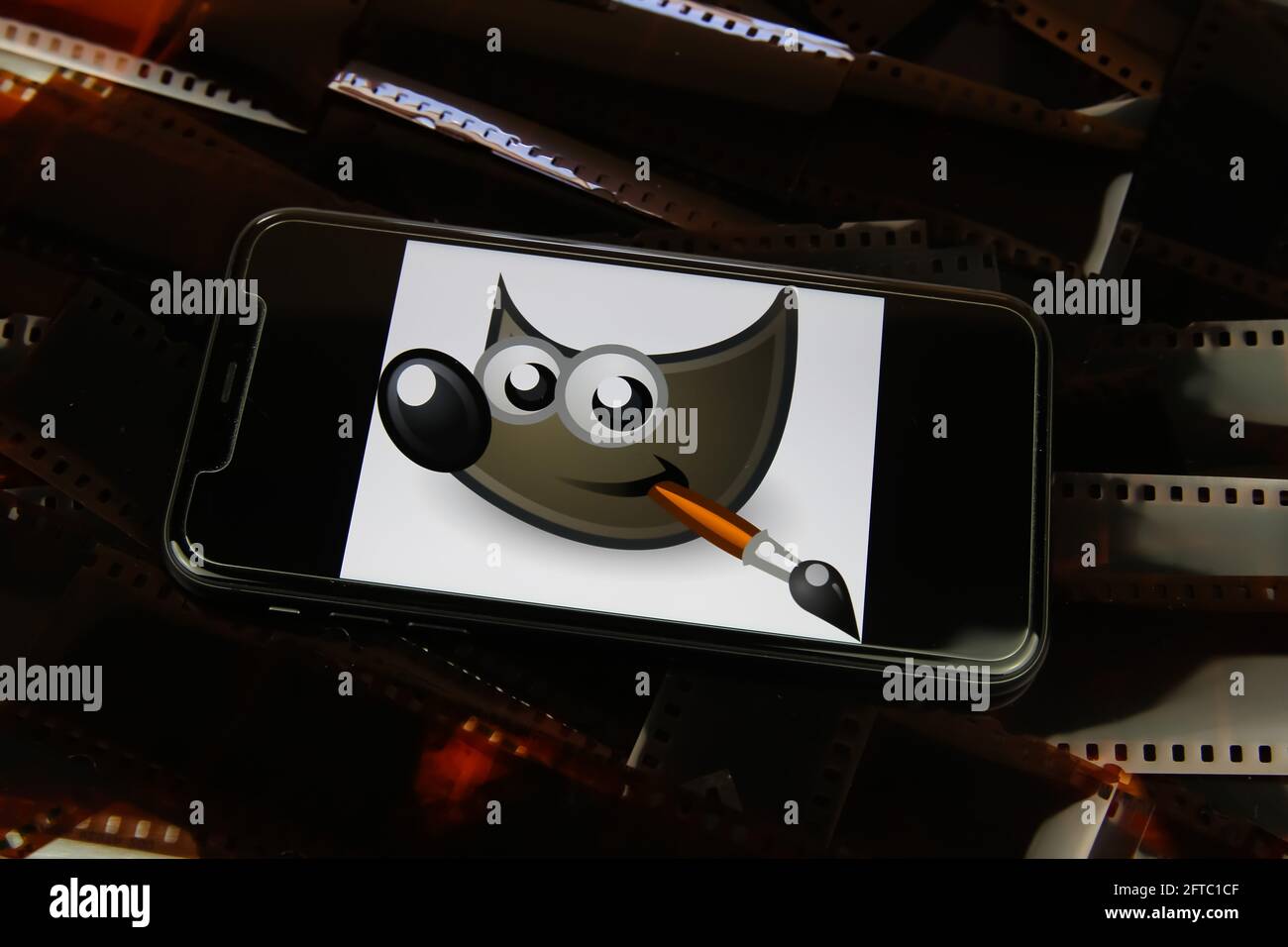 Viersen, Germania - 9 maggio. 2021: Primo piano dello smartphone con logo del programma di editing di immagini gimp su strisce di pellicola negative Foto Stock