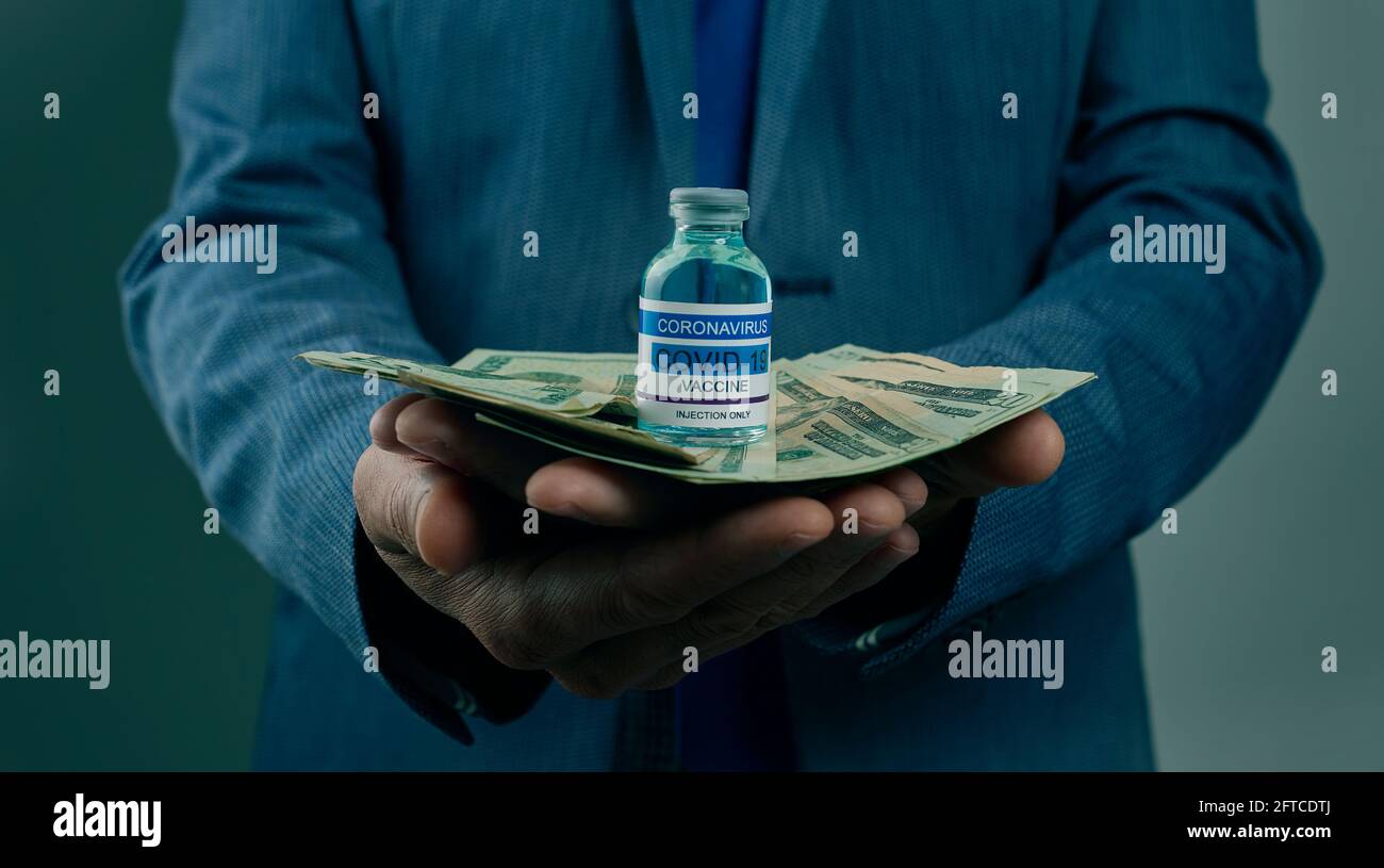 un giovane uomo d'affari ha una bottiglia simulata di vaccino covid-19 e. un mazzo di banconote in dollaro nelle sue mani Foto Stock