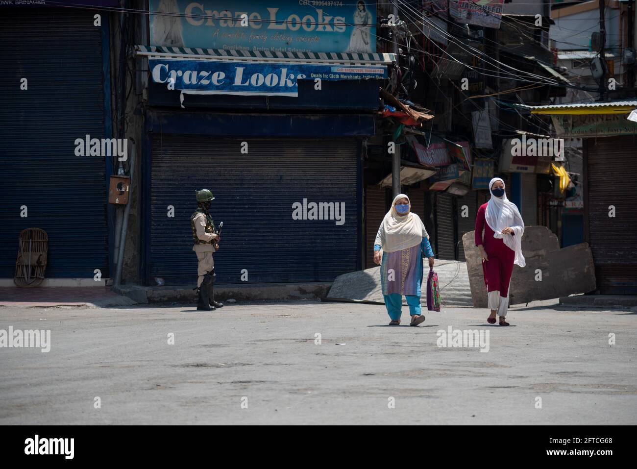 Srinagar, India. 21 Maggio 2021. Le donne di Kashmiri che indossano le maschere facciali come precauzione contro la diffusione del covid-19 camminano oltre un allarme paramilitare indiano in piedi in un mercato chiuso durante le restrizioni in Lal chowk.The autorità su Venerdì stretto il coprifuoco Covid-19 nel distretto di Srinagar alla vigilia del anniversario della morte di Mirwaiz Molvi Mohammad Farooq e Abdul Ghani Lone, che si sta marcando il 21 maggio in Kashmir. Credit: SOPA Images Limited/Alamy Live News Foto Stock