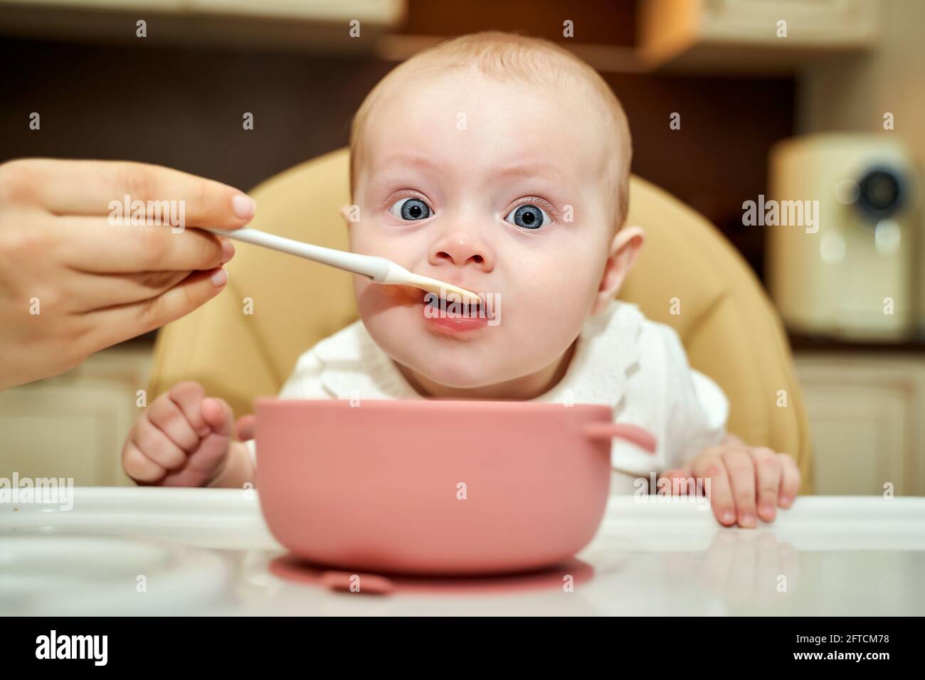 un bambino con gli occhi blu è alimentato da una madre con un cucchiaio. la prima esca. 6 mesi Foto Stock