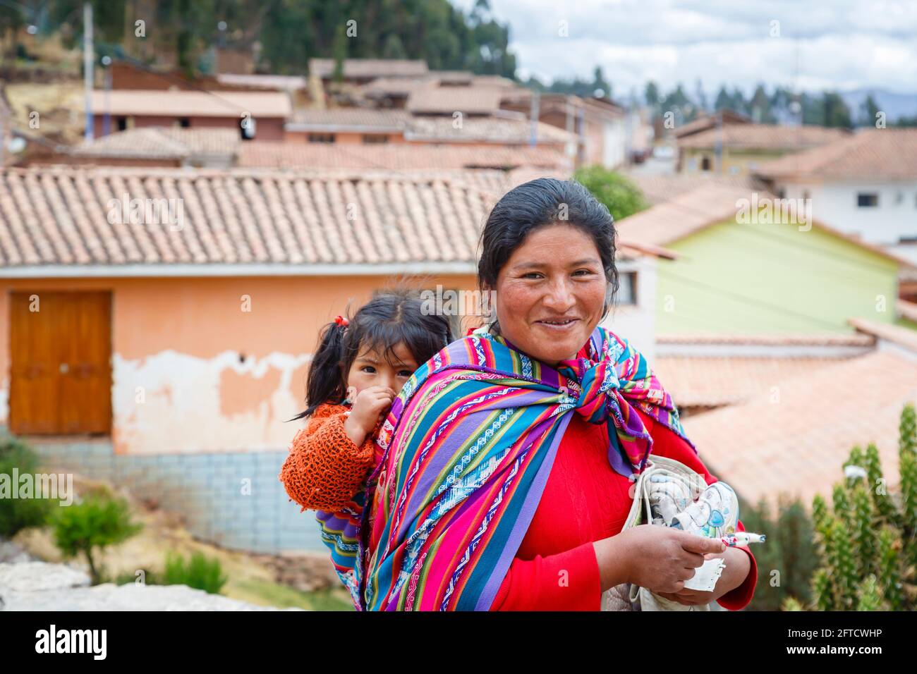 Una donna locale di Quechua porta la figlia in una papiosa di scialle a Chinchero, un villaggio andino rustico nella Valle Sacra, Urubamba, Cusco, Perù Foto Stock