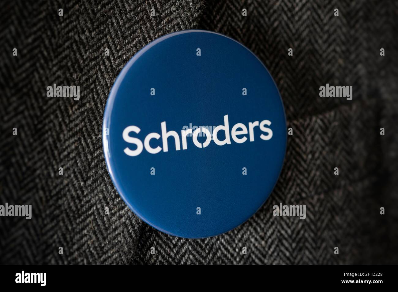 Un badge a bottone con il logo della Schroders Bank fissato a una giacca da tuta. Foto Stock