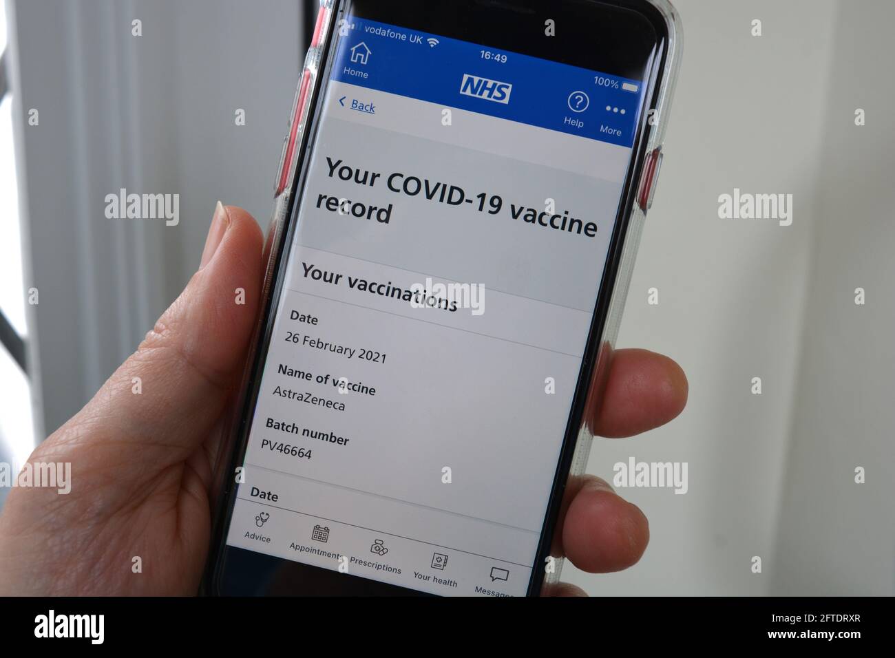 Donna che tiene il telefono cellulare con l'app NHS sullo schermo a. controllare lo stato e la registrazione del vaccino Foto Stock