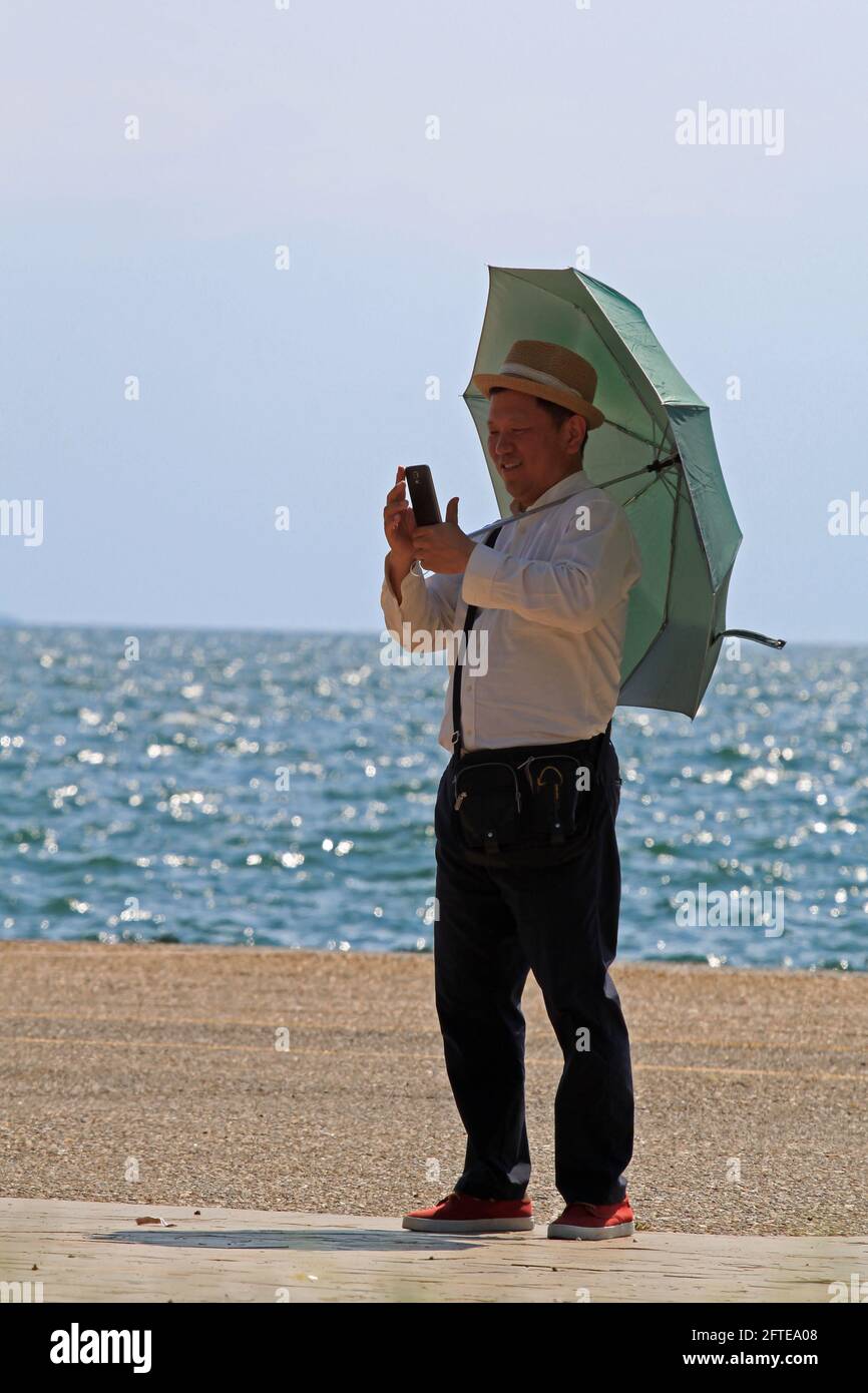 Un uomo cinese in piedi e guardando un cellulare Salonicco (Grecia) – 9 agosto 2015: Un uomo cinese in piedi su una strada di mare a Salonicco Foto Stock