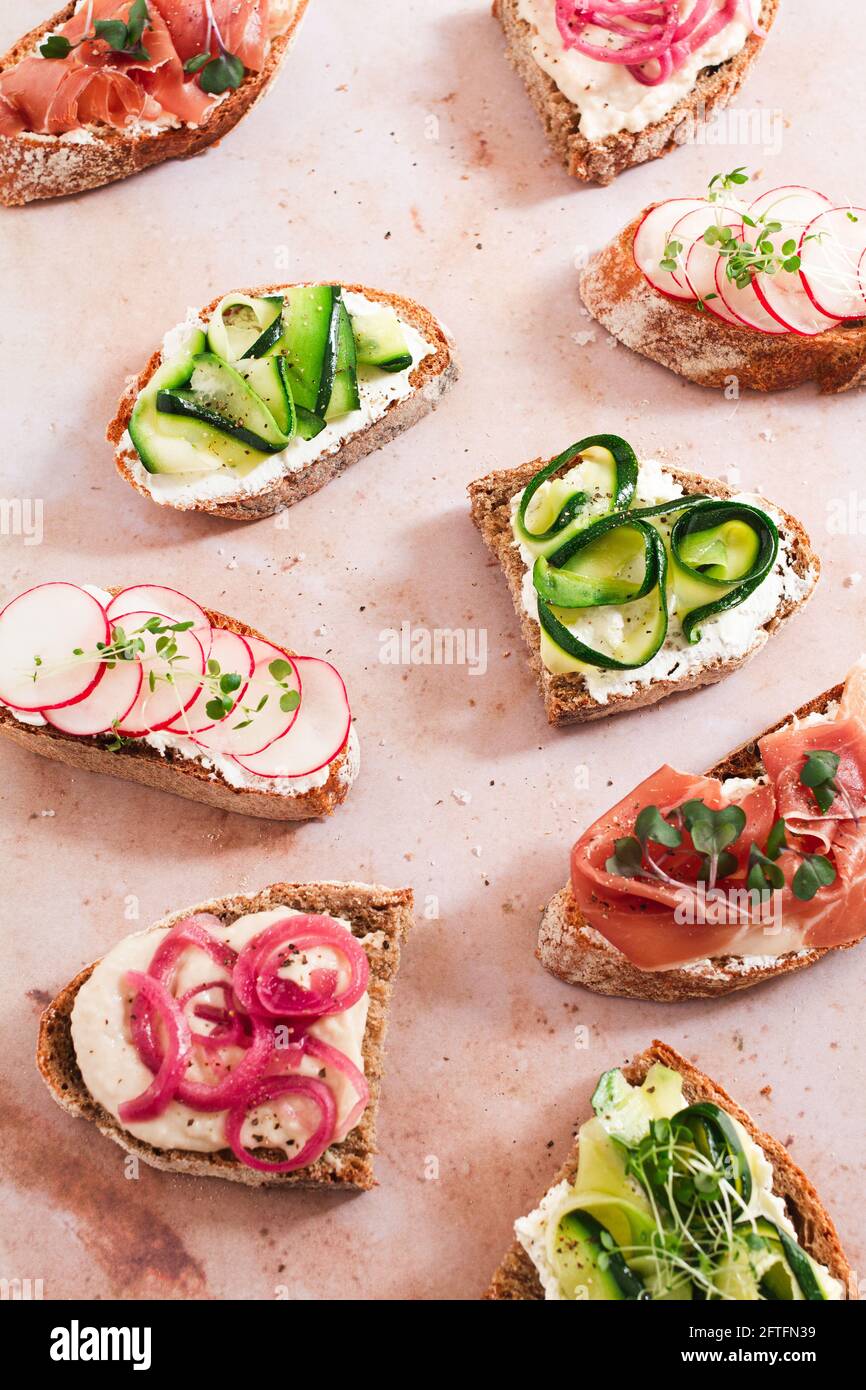 Selezione di tartine salate. Affumgasbord di fette di pane ricoperte di: Prosciutto di Serrano, fette di zucchine, fette di rafano, purea di fagioli, cipolla rossa sottaceto. Foto Stock