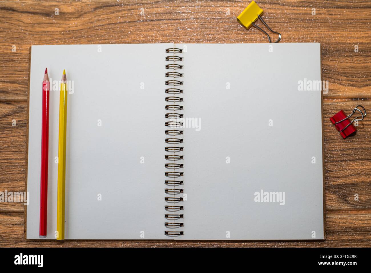 Notebook con foglio bianco aperto sul tavolo, accanto ai materiali di consumo rosso e giallo: Matite e clip per rilegatori Foto Stock