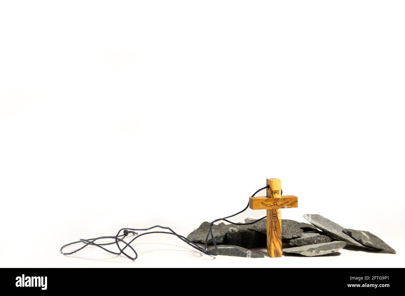 Collana di crocifisso di legno di fronte ad un piccolo mucchio di rocce su sfondo bianco Foto Stock