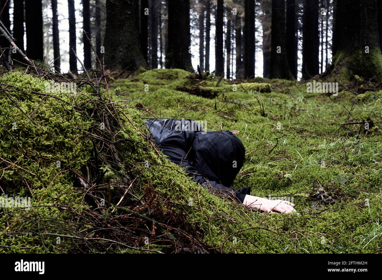 Un omicidio, concetto di crimine di un uomo incappucciato, faccia giù in una foresta scura in una giornata buia e bagnata Foto Stock