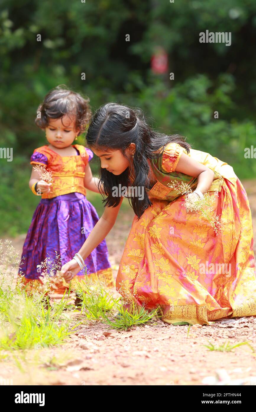 Bambini sudIndiani che indossano bella gonna lunga abito tradizionale e blusa, stropicciando i fiori di erba capelli ondulati, sfondo verde. Foto Stock