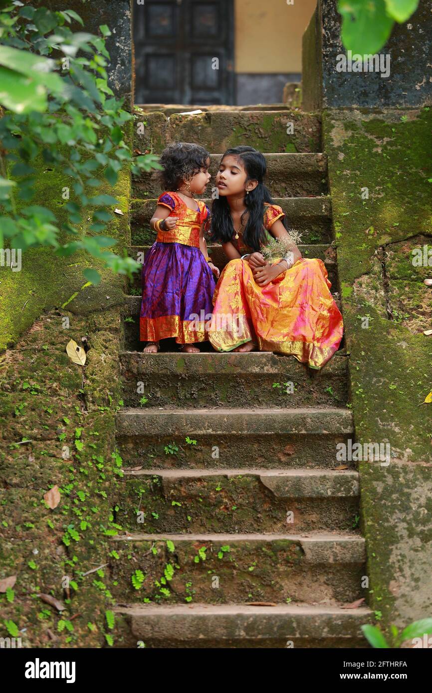 Bambini sudIndiani che mostrano diverse espressioni, indossando bella tradizionale abito gonna lunga e blusa, seduta sui lunghi passi di una casa Foto Stock