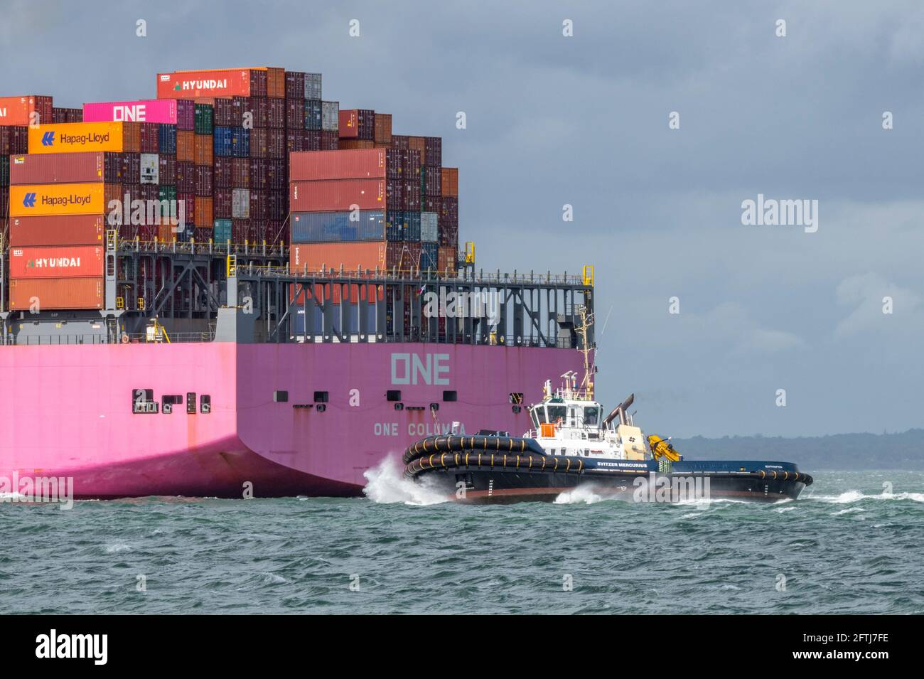 una grande nave containere una columbia che trasporta via mare contenitori che si avvicina al porto di southampton ormeggia con un rimorchiatore per l'assistenza nel solent. Foto Stock