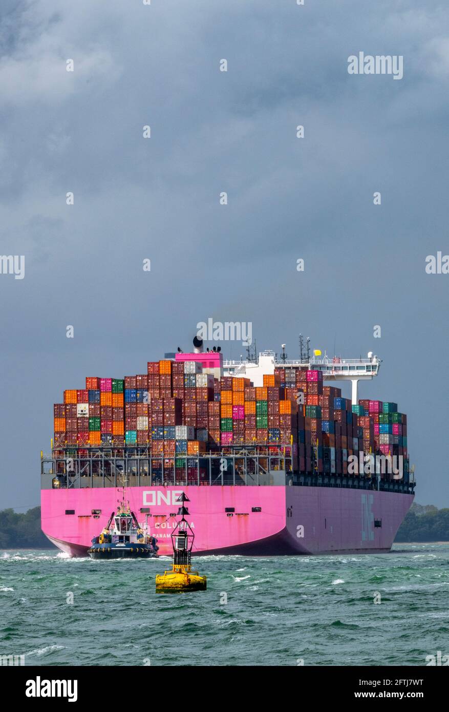 una grande nave containere una columbia che trasporta via mare contenitori che si avvicina al porto di southampton ormeggia con un rimorchiatore per l'assistenza nel solent. Foto Stock