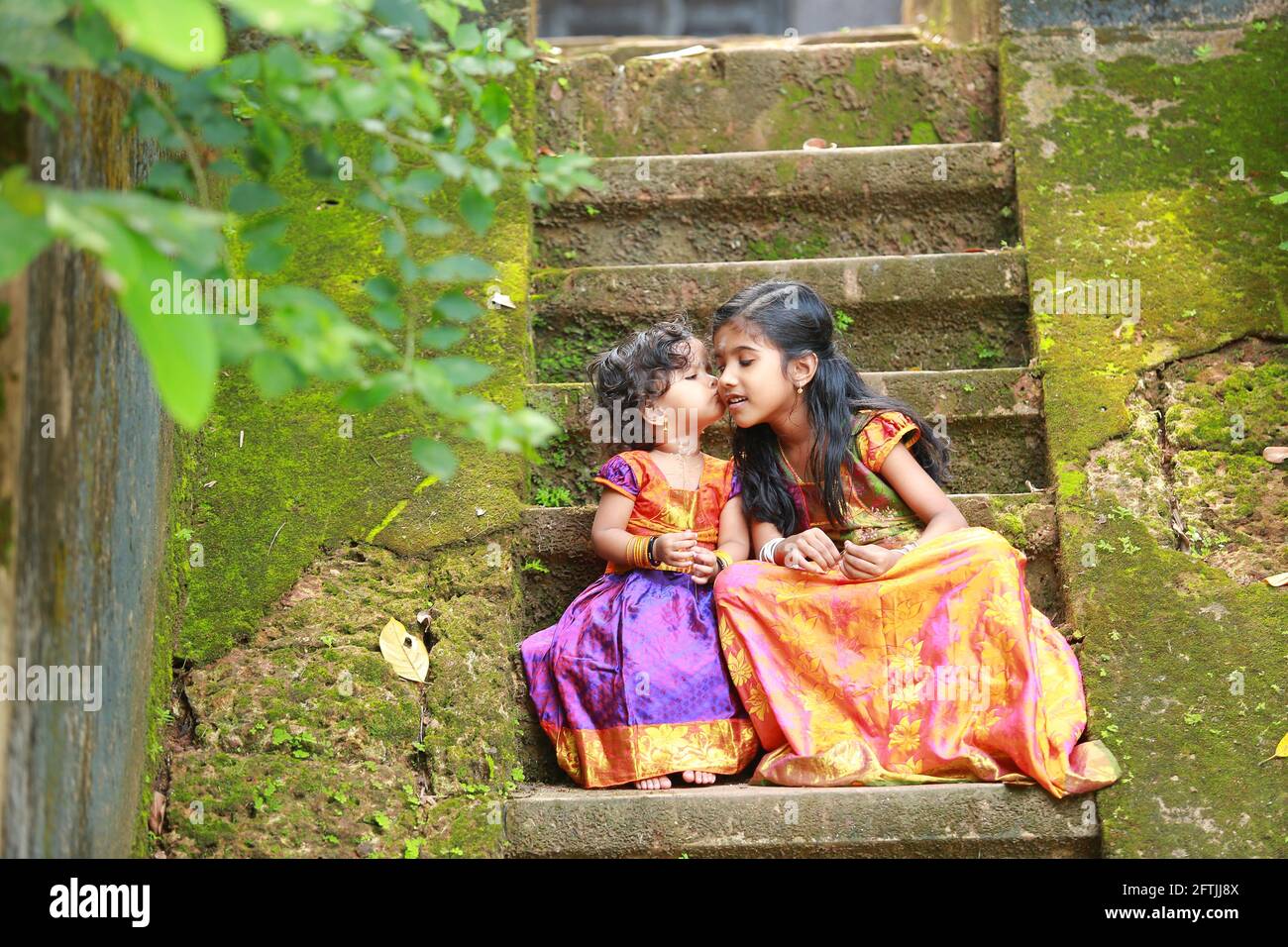 Sud indiano ragazza bambini indossando bella abito tradizionale gonna lunga e blusa, seduta sui lunghi gradini di una casa coperta con fungo verde muschio Foto Stock