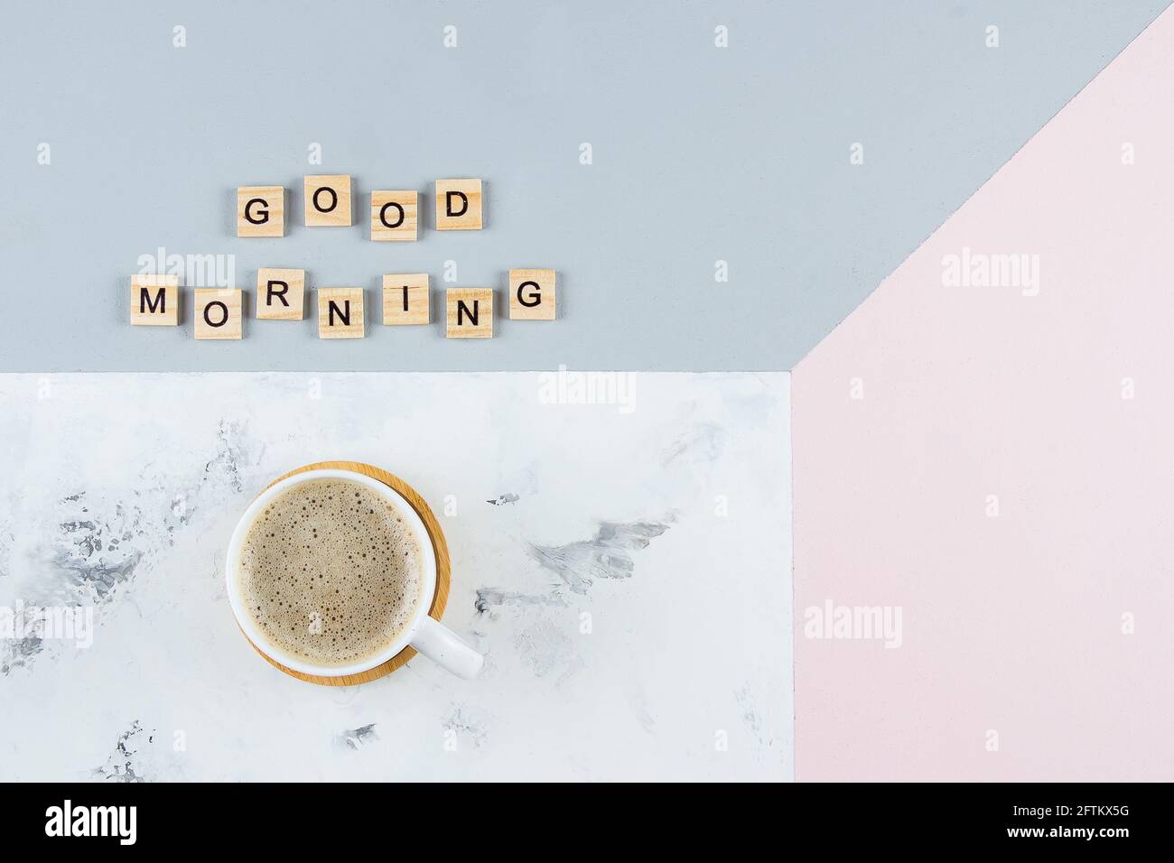 Buona colazione del mattino di concetto minimo. Tazza di caffè e testo buon mattino scrittura di lettere in legno su sfondo tricolore. Disposizione piatta, spazio copia, t Foto Stock