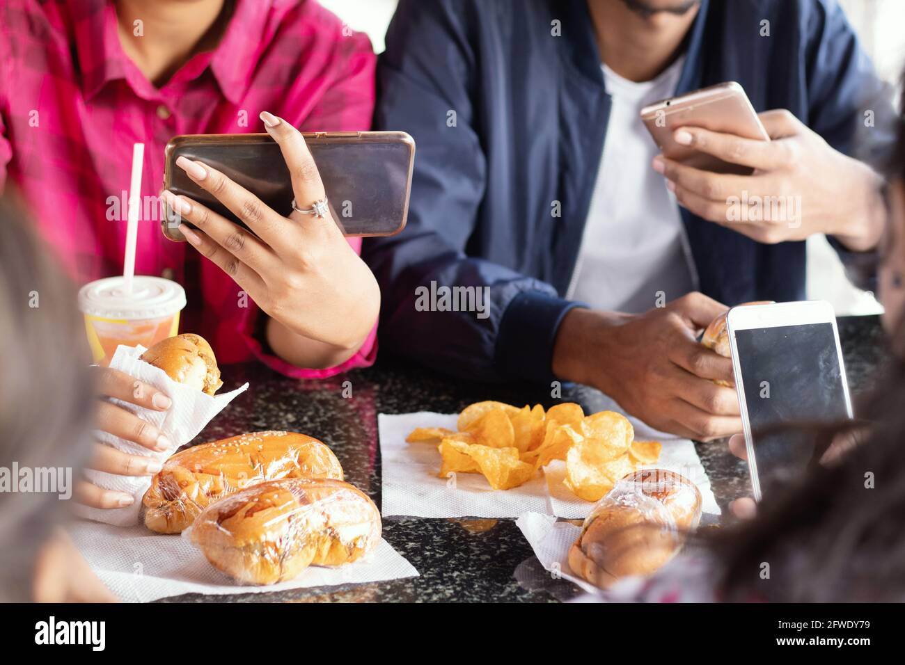 Gruppo di persone irriconoscibili che si sono occupate di dispositivi mobili mentre si mangiano spuntini insieme al ristorante - concetto di millennial che hanno cibo spazzatura, dipendenza telefonica Foto Stock