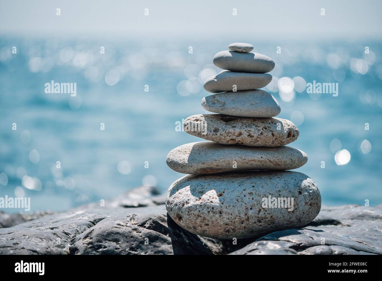 Equilibrata piramide di ciottoli sulla spiaggia in una giornata di sole. Abstract Sea bokeh sullo sfondo. Messa a fuoco selettiva. Pietre Zen sulla spiaggia di mare, meditazione Foto Stock
