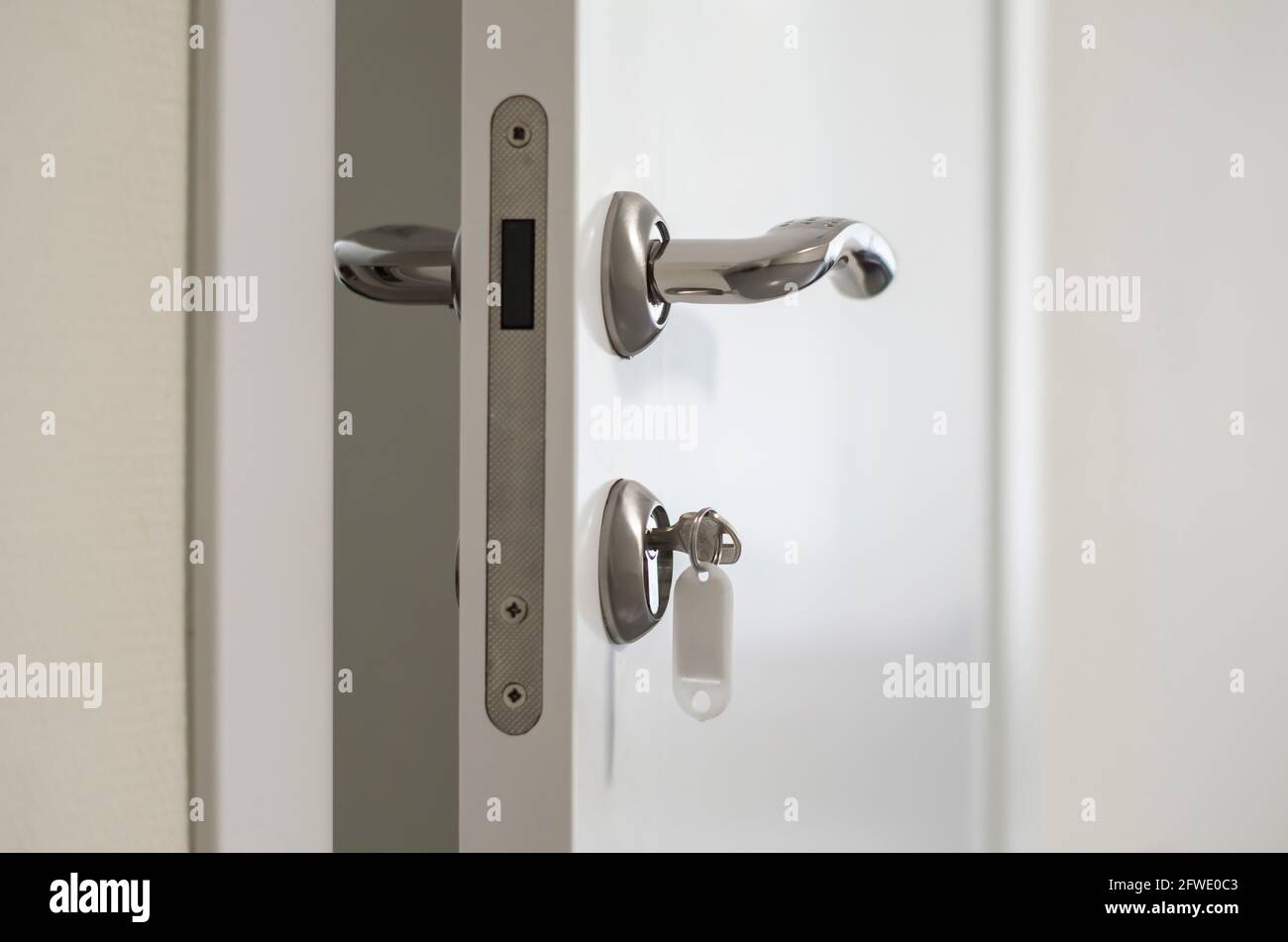 Porta bianca socchiusa con maniglie in argento e chiave nella serratura Foto Stock