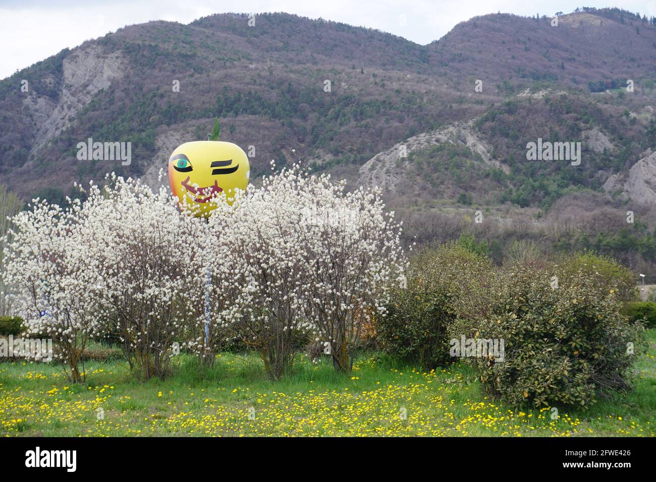 colorata scultura di mela con un volto felice sopra gli alberi bianchi in fiore su una rotonda vicino serre ponçon, francia Foto Stock