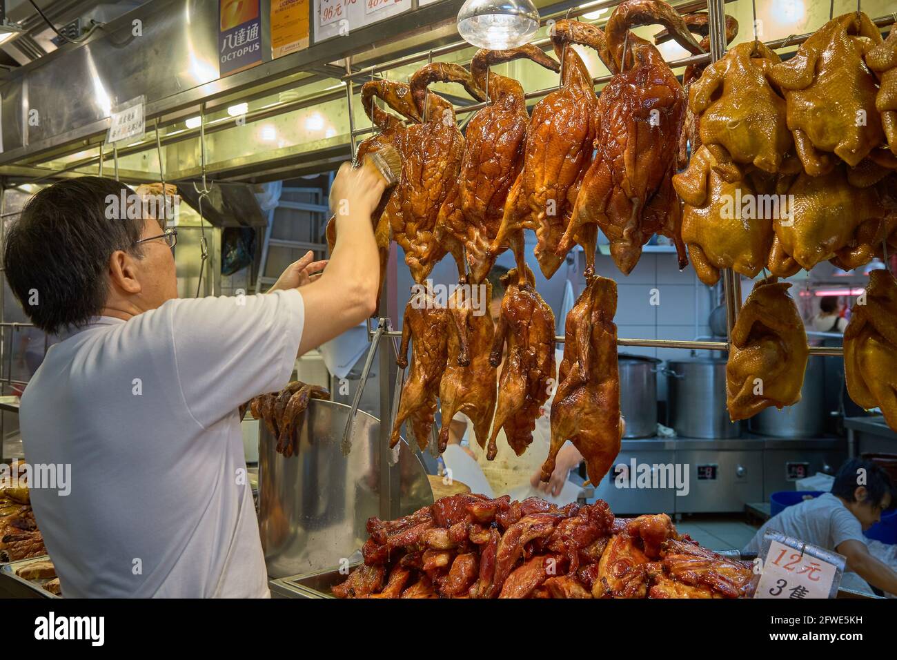 Un negoziante che prepara cibi cotti in vendita presso la sua bancarella di cibo nel mercato Tai Yuen di Hong Kong. Foto Stock