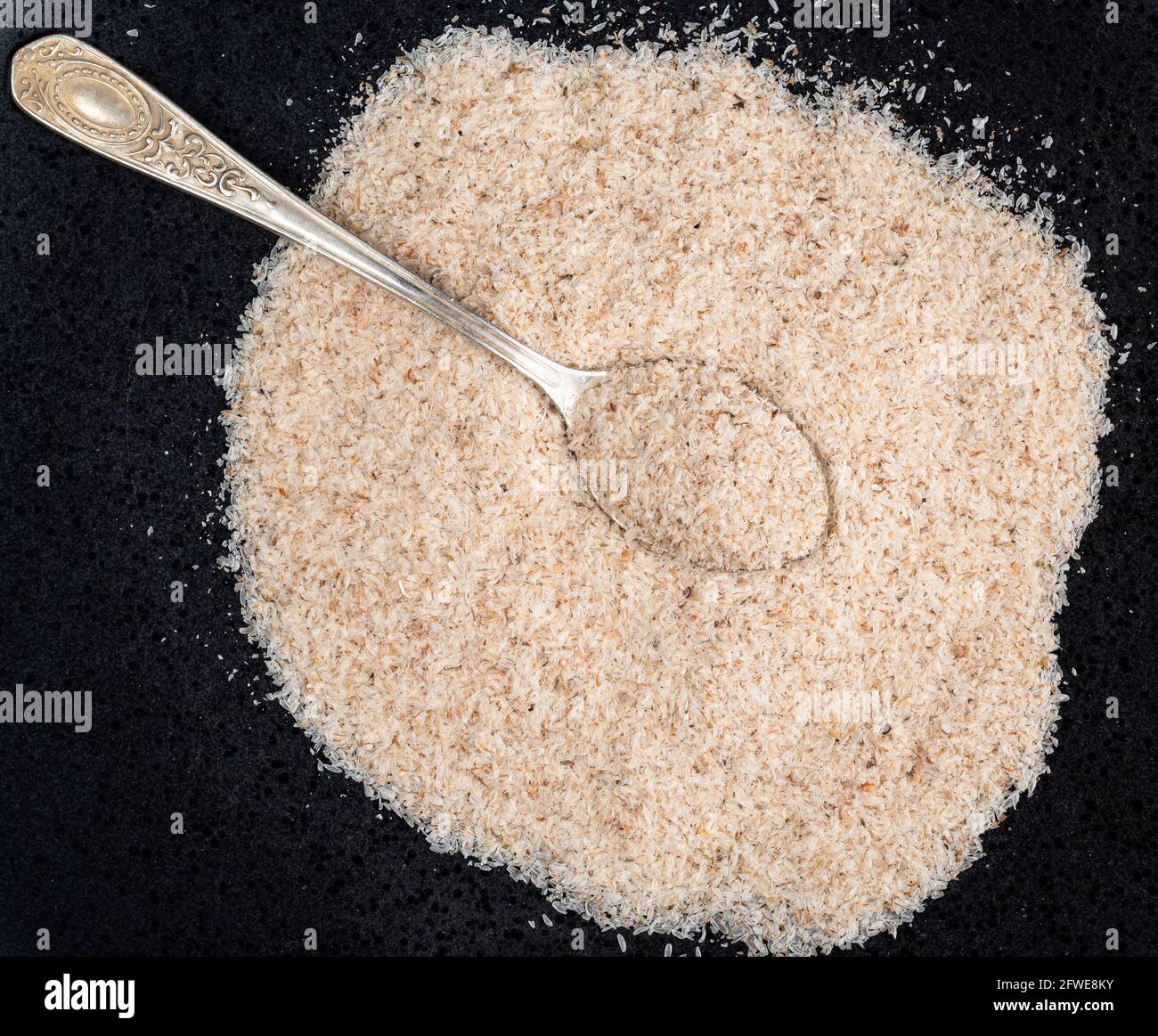 Vista dall'alto del cucchiaino d'argento in buccia di Psillio su nero piastra Foto Stock