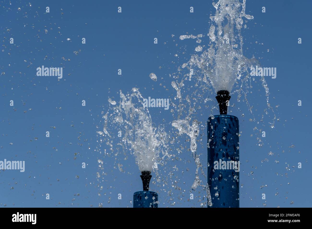 Due sprinkler blu per il parco acquatico che spruzzano acqua sopra per il divertimento estivo dei bambini. Foto Stock