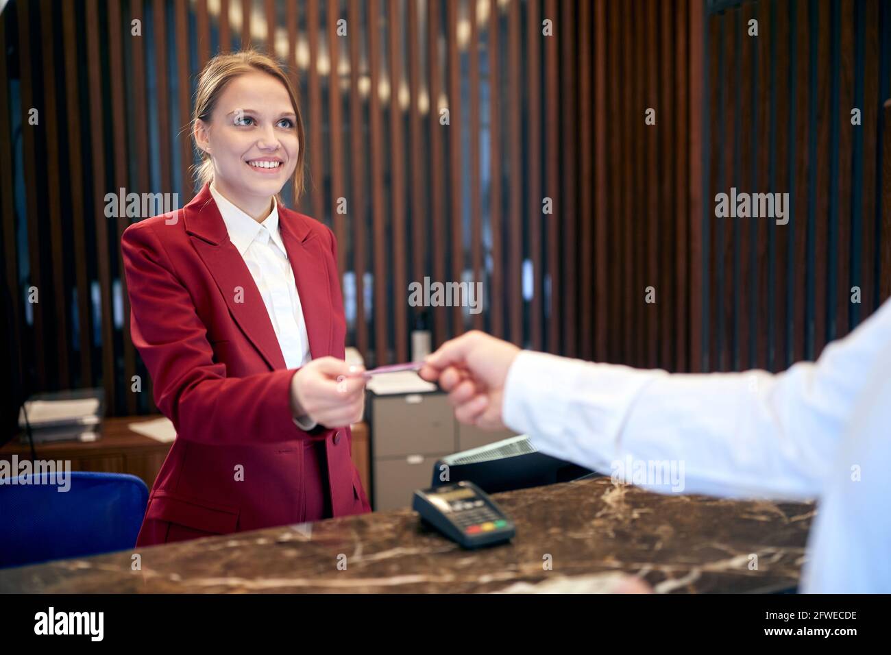 giovane addetta alla reception sorridendo ad un ospite, restituendogli la carta di credito Foto Stock