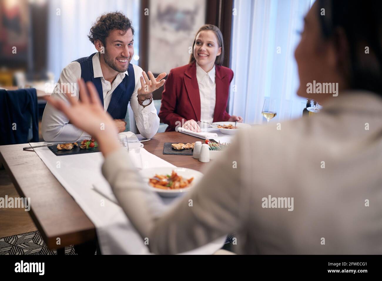 gruppo di amici caucasici che pranzano al ristorante, parlano, sorridono. Foto Stock