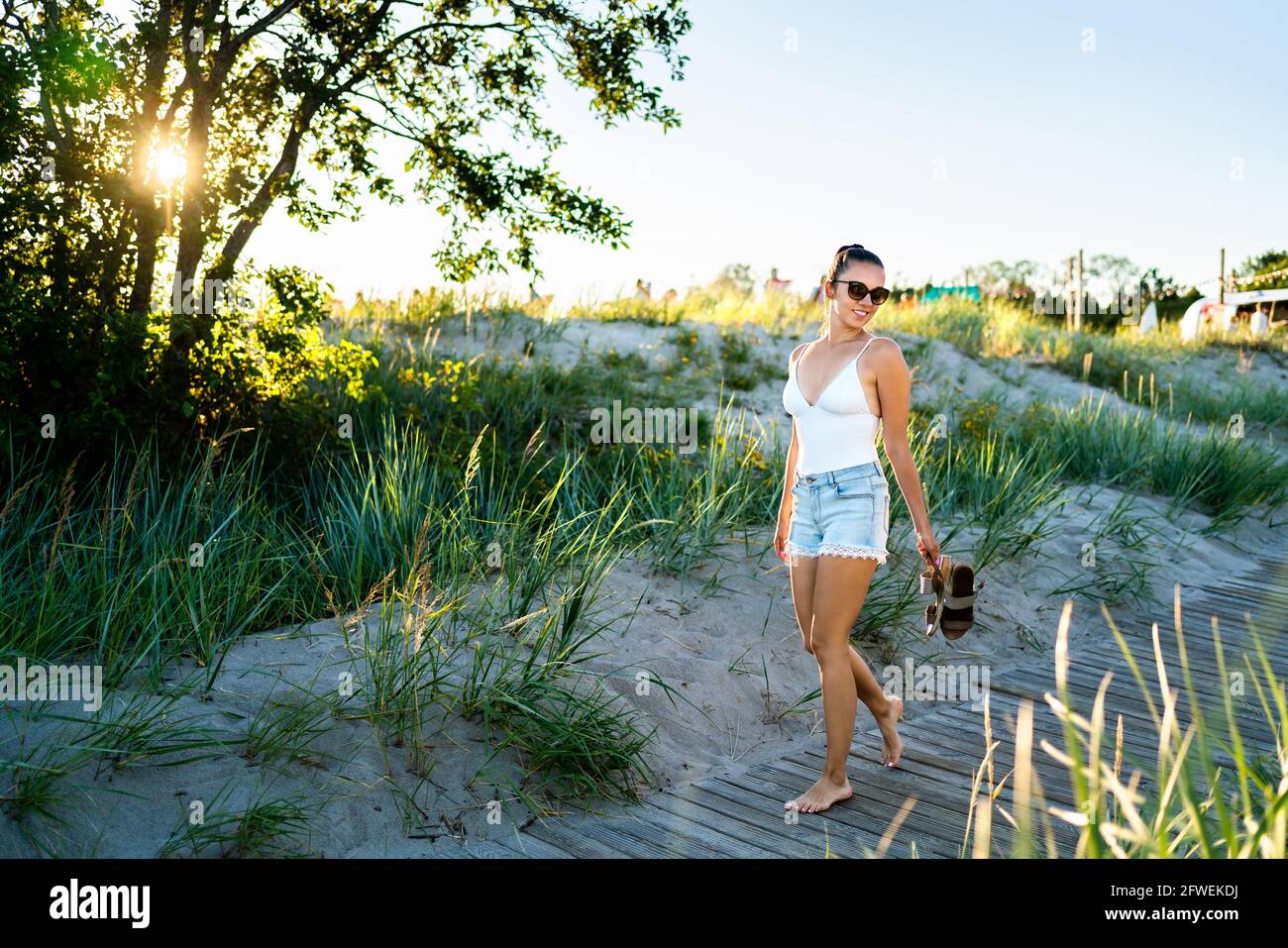 Vibrazioni estive! Giovane donna fresca che gode la vita. Felice bella ragazza a piedi sulla spiaggia lungomare al tramonto. Perfetto stile di vita caldo del fine settimana. Estate alla moda. Foto Stock