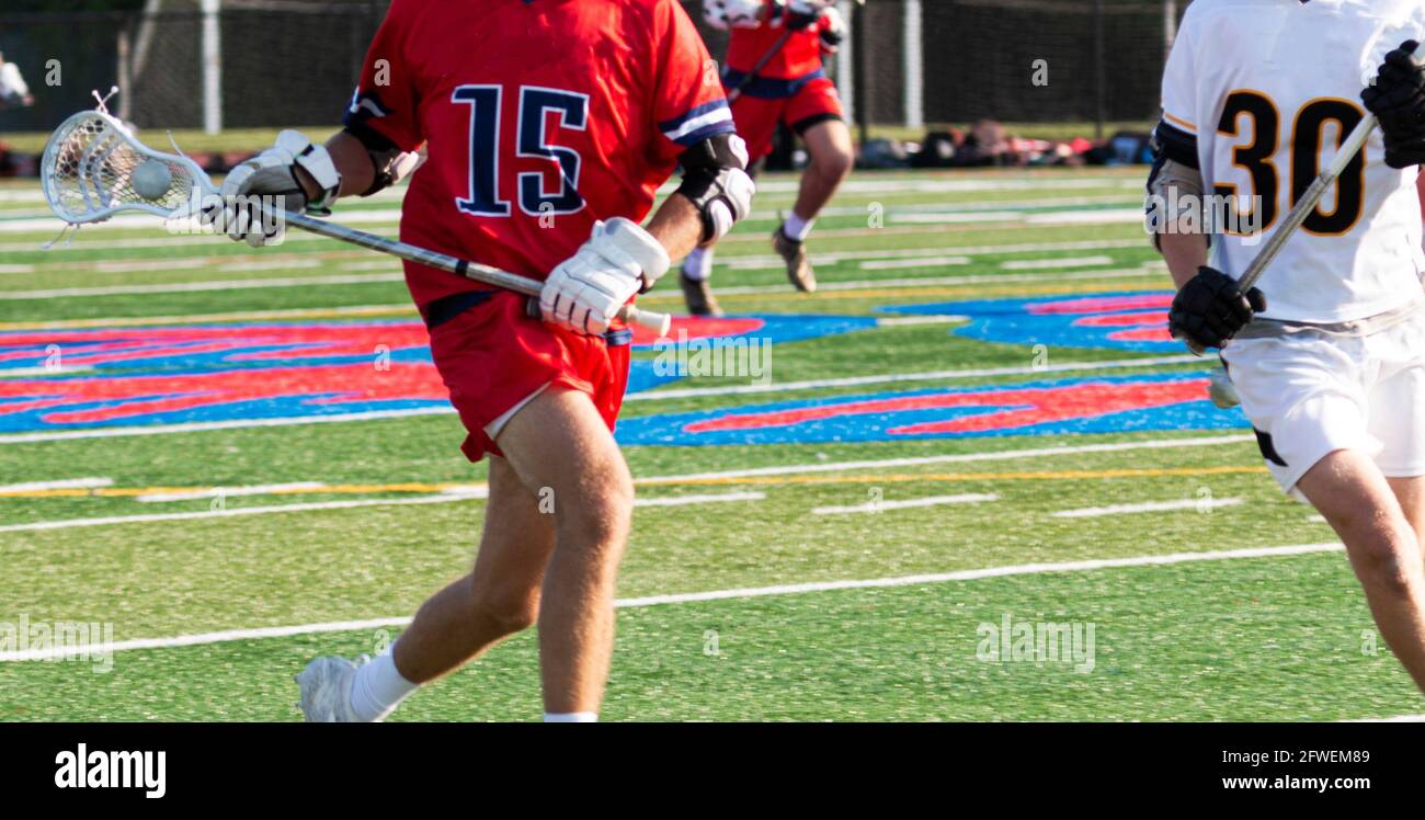 Un giocatore di lacrosse della scuola superiore che porta la palla con il suo bastone mentre corre sul campo durante una partita su un campo di erba medica. Foto Stock