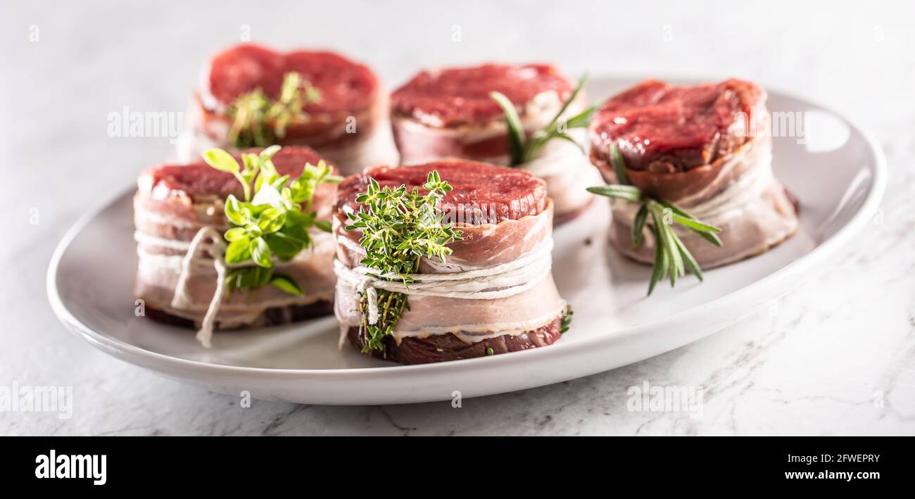 Bistecche crude avvolte con pancetta ed erbe fresche su un piatto. Foto Stock