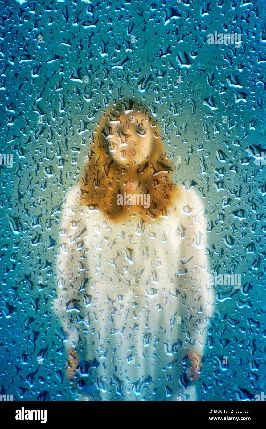 misteriosa ragazza in abito bianco dietro un bicchiere con gocce di acqua Foto Stock