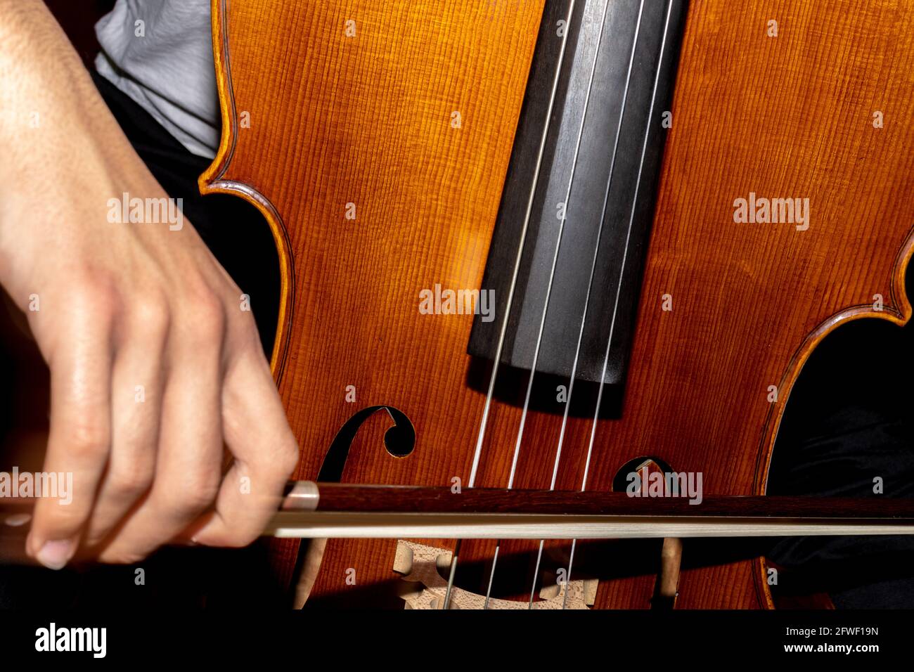 dettaglio di un uomo che suona il violoncello in legno sfregando le corde con l'arco per ottenere le note di un brano musicale classico. Foto Stock