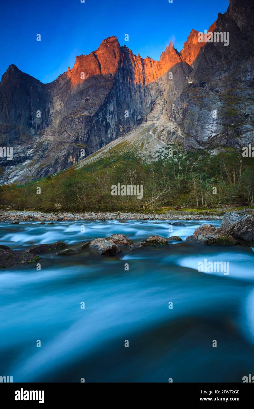 Luce mattutina con alpenglow sulle montagne e acqua in streaming nel fiume Rauma nella valle di Romsdalen, Rauma kommune, Møre og Romsdal, Norvegia. Foto Stock